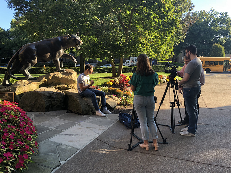 UPTV filming male speaker outside by Pitt Panther statue